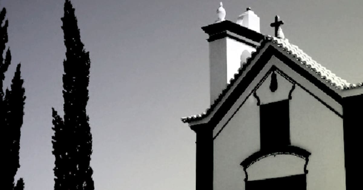 Silhueta de igreja e ciprestes ao entardecer.