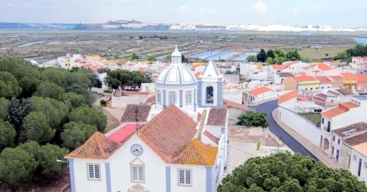 Vista aérea de vila portuguesa com igreja e rio.